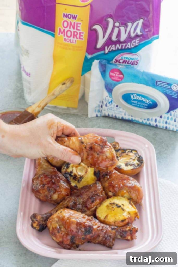 A close-up of a hand basting BBQ Peach Ginger Glazed Chicken Legs with sauce on the grill.