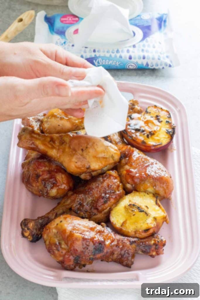 A beautifully composed shot of BBQ Peach Ginger Glazed Chicken Legs on a wooden board, with fresh peaches and ginger in the background.