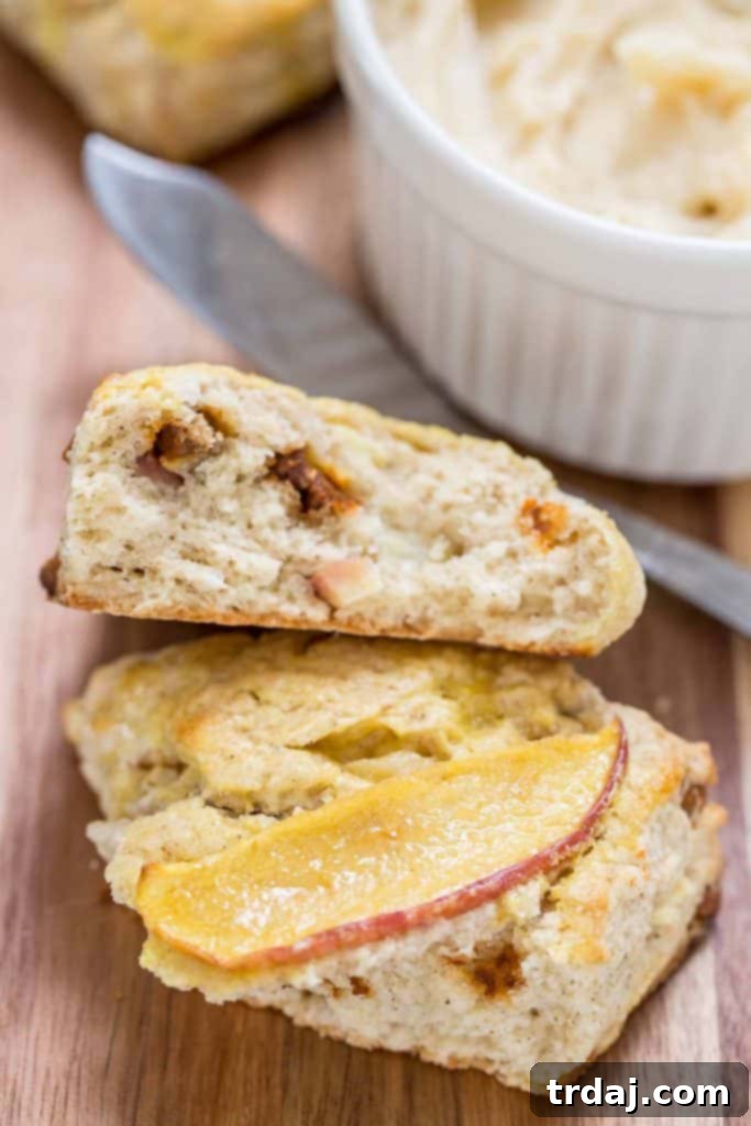 Dive into the rich flavors of Fall with these moist Apple Cinnamon Scones, enhanced by Envy apples, cinnamon chips, and decadent Maple Butter. Close-up of a cut Apple Cinnamon Scone showing the apple chunks and cinnamon chips, ready for Maple Butter