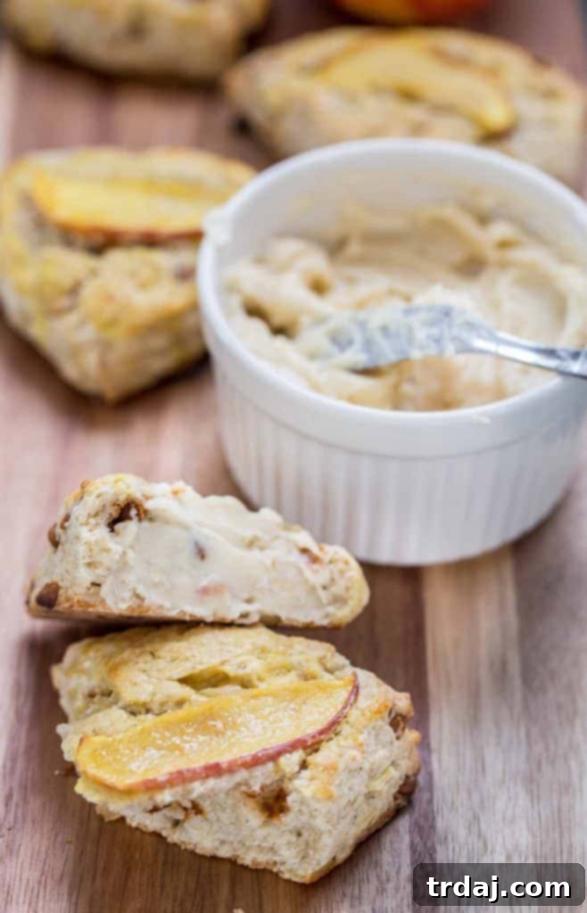 A delicious Apple Cinnamon Scone lavishly topped with rich Maple Butter, perfect for any Fall occasion. Close-up of an Apple Cinnamon Scone with Maple Butter melting over it, on a wooden board