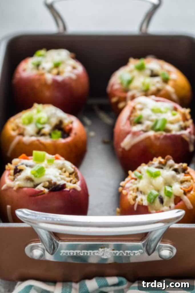 Three beautifully baked Stuffed Apples with Cheddar and Sausage in a roasting pan, ready to serve.