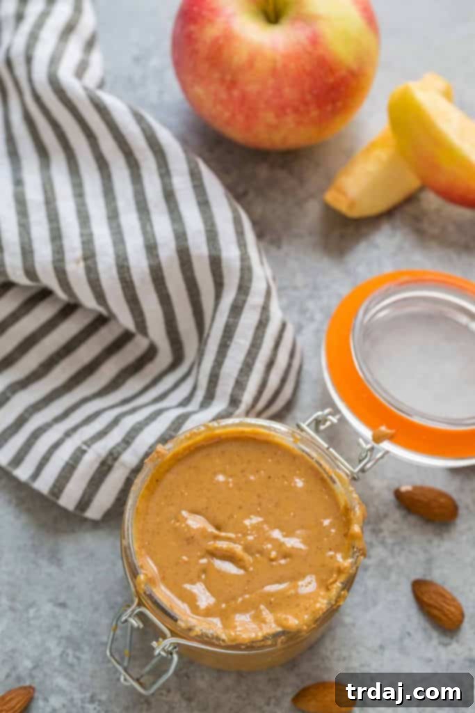 Aromatic spices combine with almonds to create a delicious Apple Chai Almond Butter that's perfectly spreadable on anything from apples to bread and everything in between! Apple Chai Almond Butter served with apple slices on a wooden board