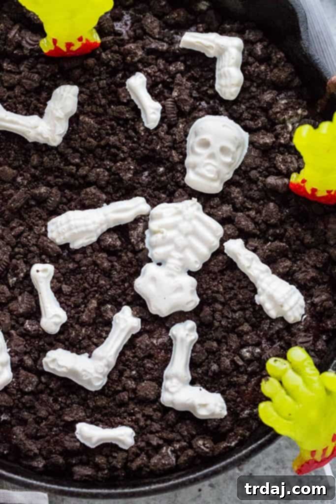 Rich and decadent skillet brownies get topped with chocolate skeletons, gummy zombie hands and 'dirt' to make spooky and delicious Halloween Graveyard Brownies! Halloween Skillet Brownies with chocolate skeletons and candy zombie hands