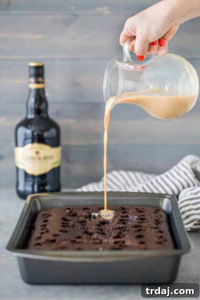 Homemade chocolate cake is soaked with Irish cream and topped with whipped cream frosting and a sprinkle of chocolate shavings for a decadent and creamy Irish Cream Poke Cake. Pouring creamy Baileys Irish Cream into the pre-poked holes of a chocolate cake, ensuring even saturation