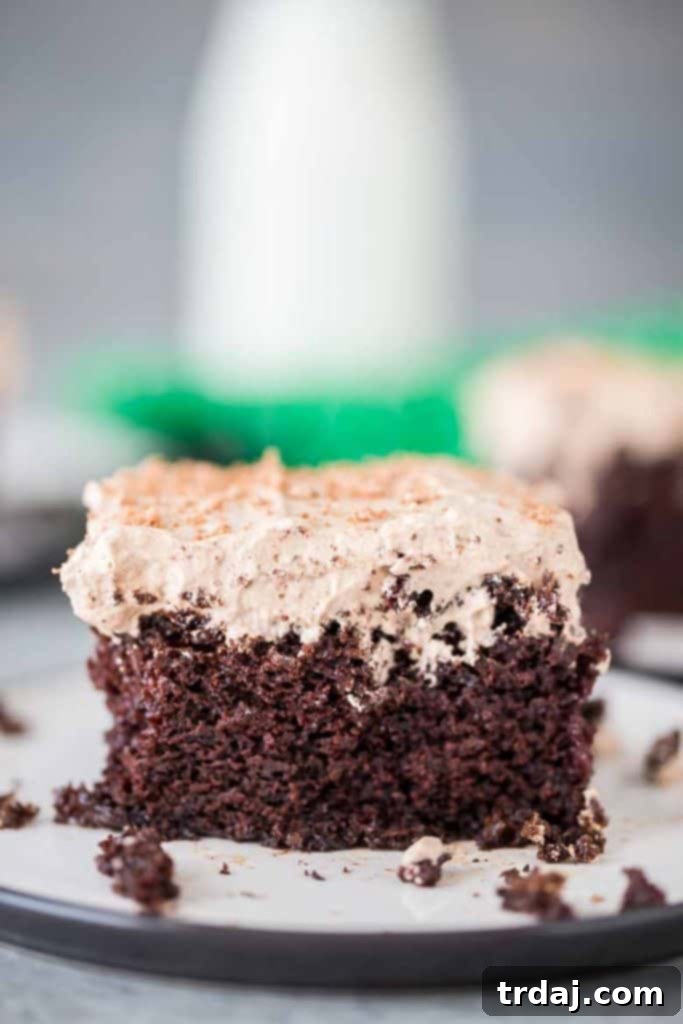 Homemade chocolate cake is soaked with Irish cream and topped with whipped cream frosting and a sprinkle of chocolate shavings for a decadent and creamy Irish Cream Poke Cake. Full view of a beautifully decorated Irish Cream Poke Cake on a serving platter, ready to be enjoyed