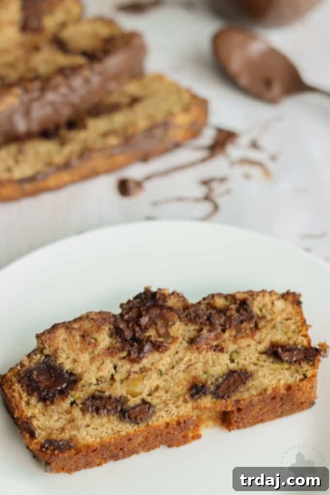 Close-up shot of a perfect slice of Chocolate Chunk Zucchini Bread, highlighting its moist texture, chocolate chunks, and subtle green flecks.