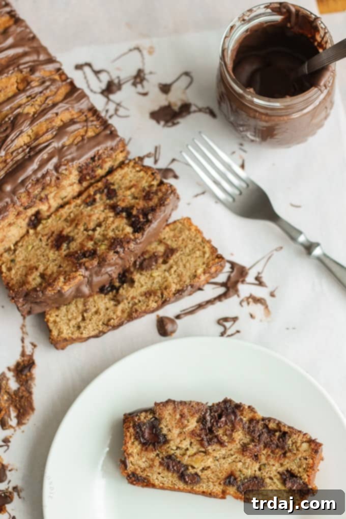 A vertical shot of a large, beautiful loaf of Chocolate Chunk Zucchini Bread, artfully drizzled with chocolate.