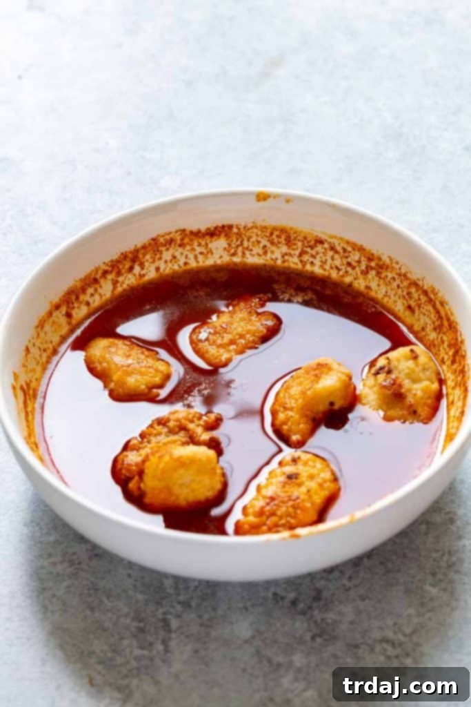 Nashville Hot Chicken Waffles Bites Cooked chicken pieces being coated in Nashville Hot sauce for waffle bites.