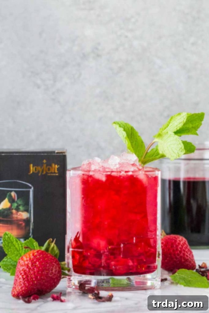 Strawberry Hibiscus Mint Julep Presentation A Strawberry Hibiscus Mint Julep cocktail in a geometrically shaped clear glass, highlighting the beverage's color and the mint garnish against a soft-focus background.