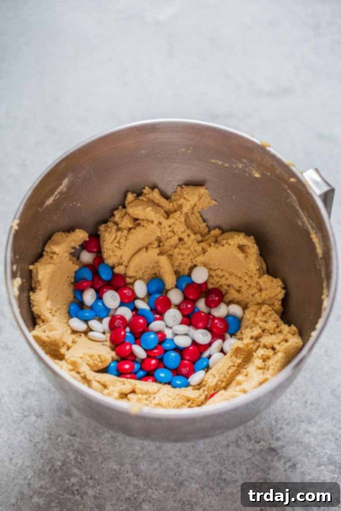 Folding M&M's candies into cookie dough using a spatula, ensuring even distribution for a festive treat.