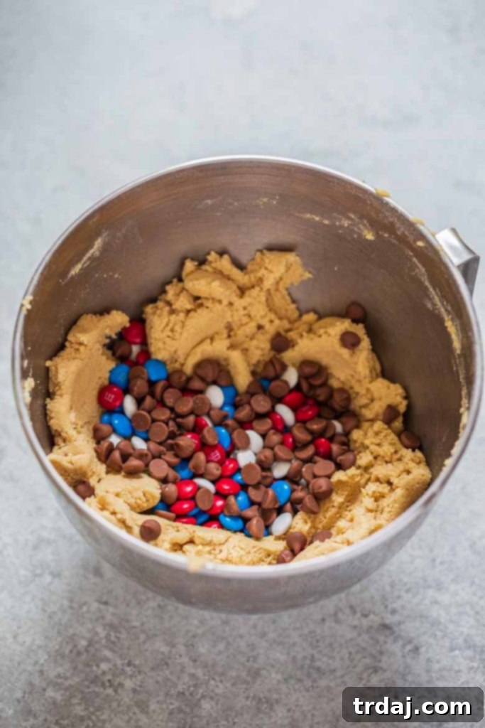 Folding chocolate chips and colorful sprinkles into edible cookie dough, creating a visually appealing and delicious mixture.