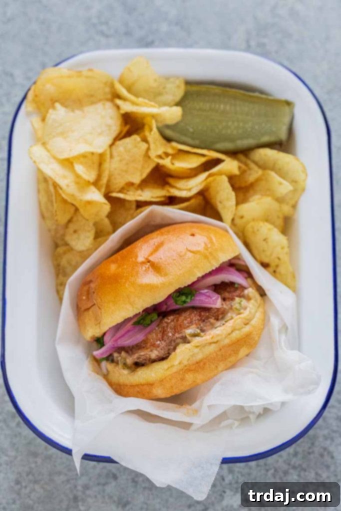 A close-up of a fully assembled Chile Chorizo Burger, showcasing the vibrant toppings and juicy patty