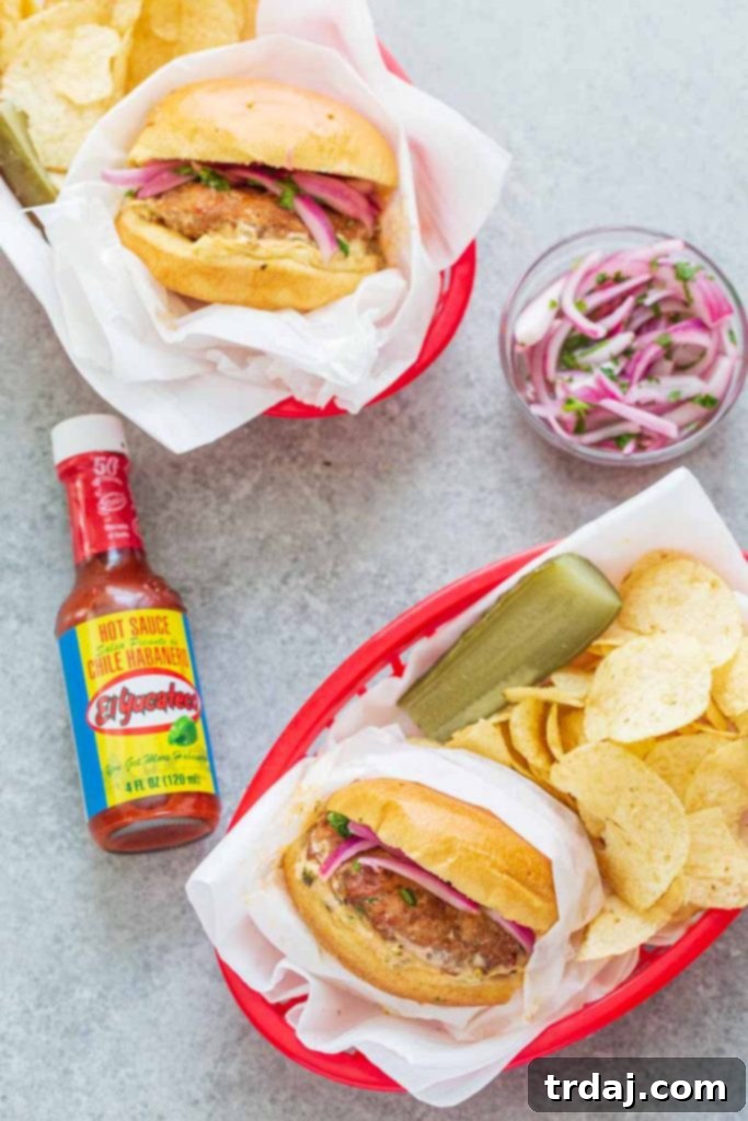Two Chile Chorizo Burgers on a bun, with toppings, on a wooden board