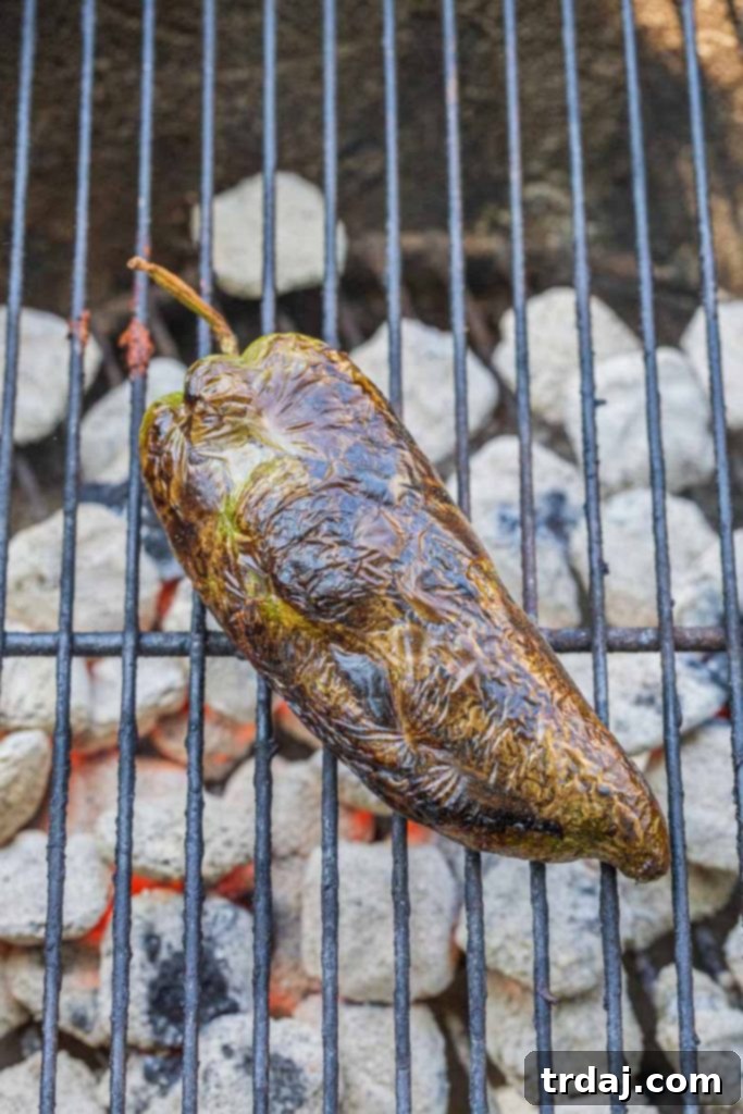 A poblano pepper charring directly over a grill flame, turning black and blistered