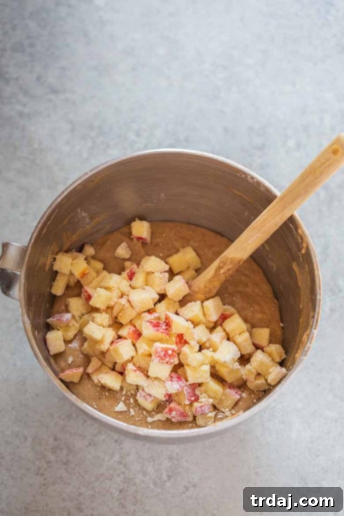 Apples being folded into banana bread batter with a spatula.