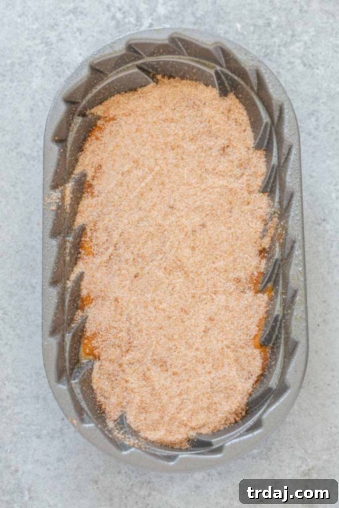 Pumpkin bread batter in a loaf pan with a generous layer of cinnamon sugar sprinkled on top, ready for baking.
