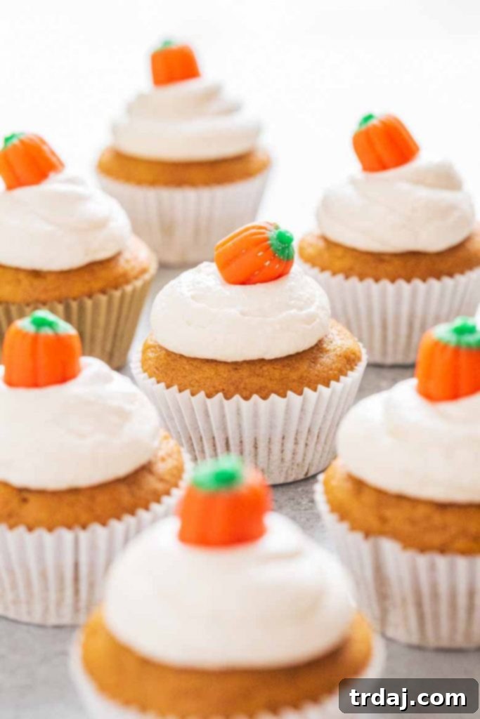 Three beautifully decorated pumpkin cupcakes, garnished with candy corn pumpkins and festive sprinkles.