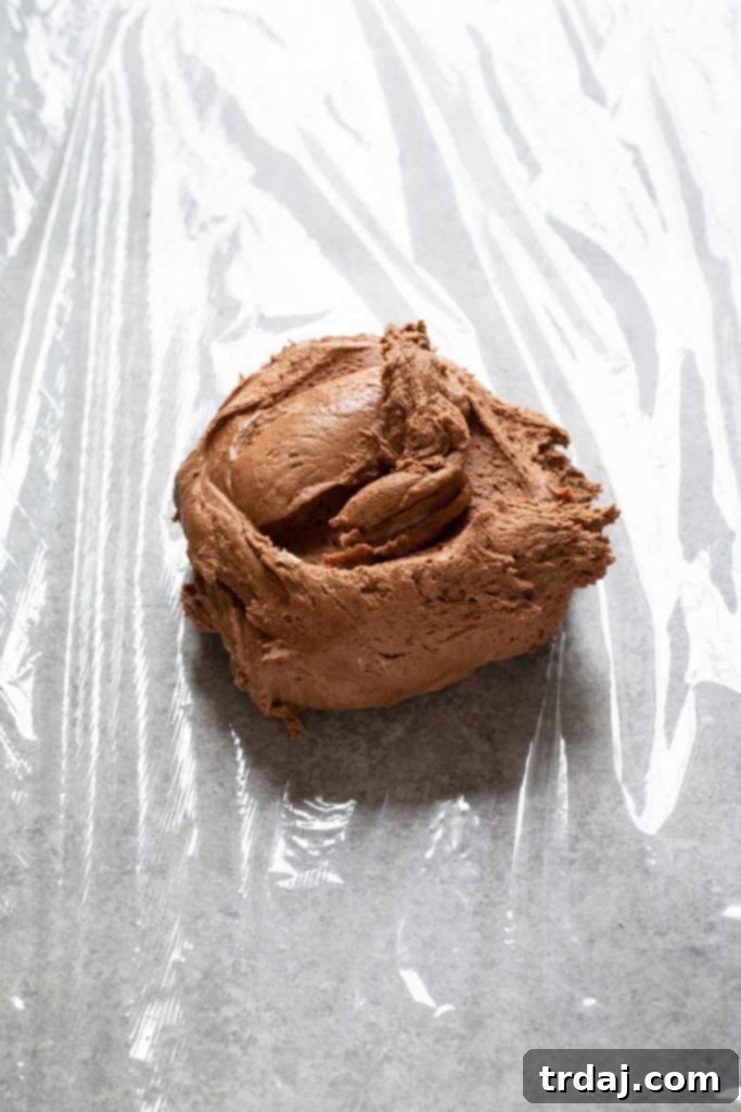 Death by Chocolate Dessert Ball is a chocolate lover's dream! Filled with chocolate sauce and rolled in mini chocolate chips, it's the perfect dessert to serve for a party! Placing the chocolate cheese ball mixture onto plastic wrap before shaping and chilling for the Death by Chocolate Dessert Ball.