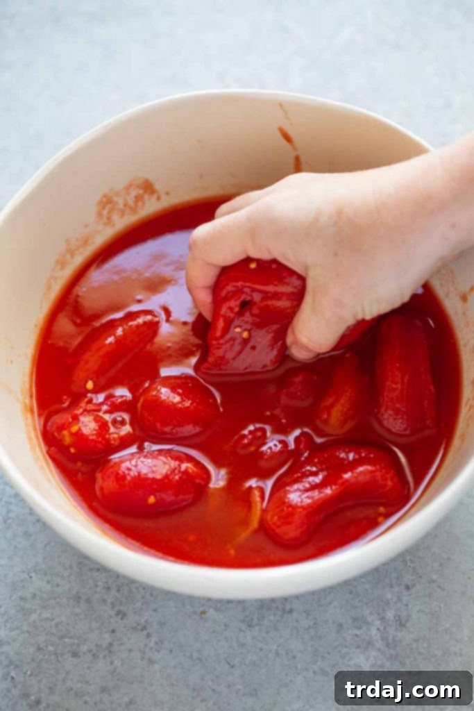 Place San Marzano tomatoes into a bowl and crush with your hands