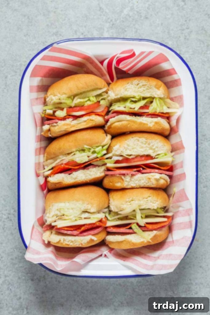 A top-down shot of a tray of freshly made Italian Sandwich Sliders, with vibrant green lettuce, red tomatoes, and sliced meats visible.