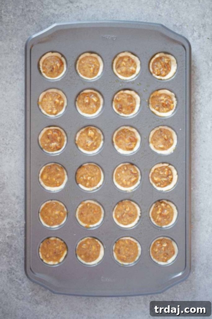 Spoonful of pecan tassie filling being added to the dough in a mini muffin tin