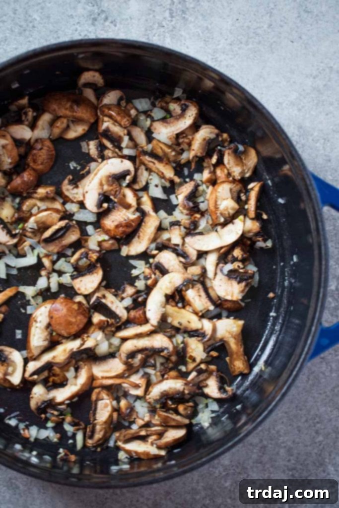 A skillet filled with sautéed garlic, onions, and mushrooms cooking in butter, forming the flavorful base for the homemade cream of mushroom soup.