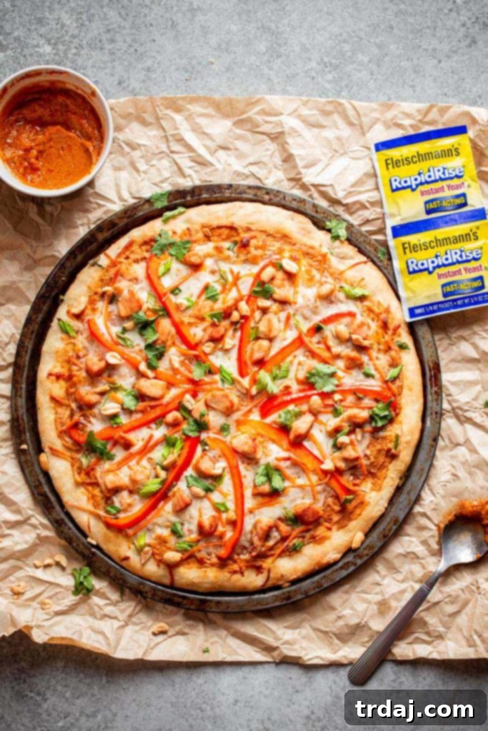 A vibrant and delicious Thai Chicken Pizza, whole and ready to be sliced, showcasing all its fresh toppings.