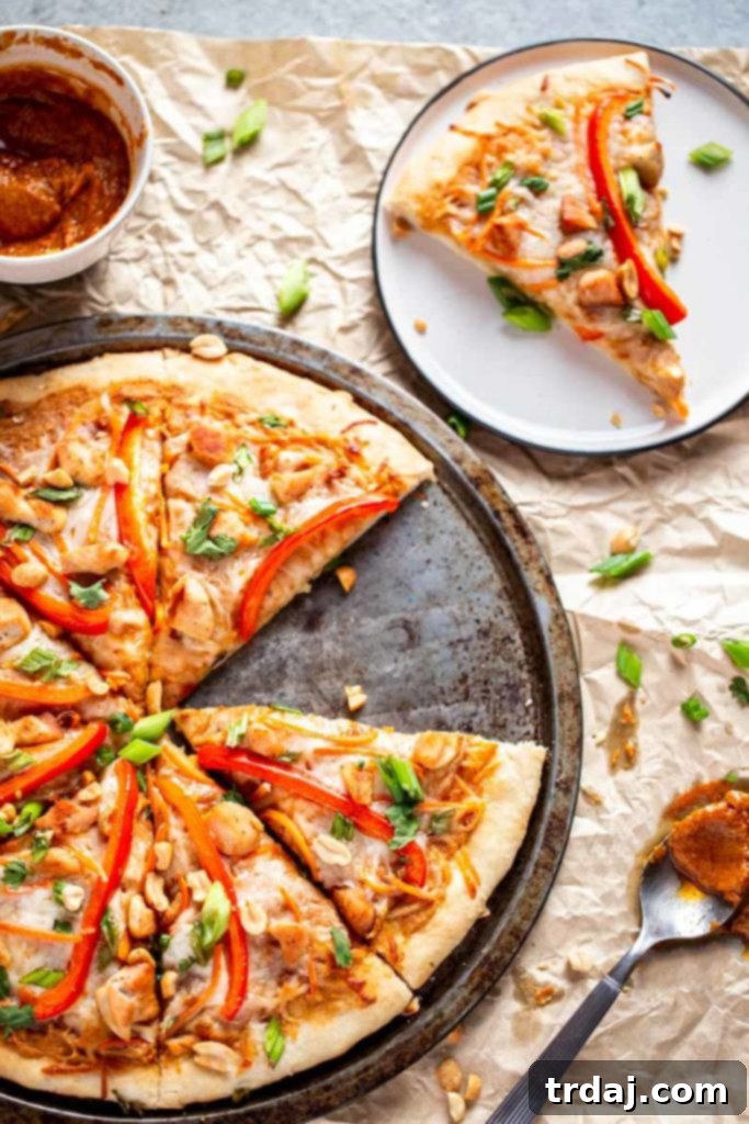 A slice of freshly baked Thai Chicken Pizza accompanied by a small bowl of homemade peanut sauce, ready for a delicious meal.
