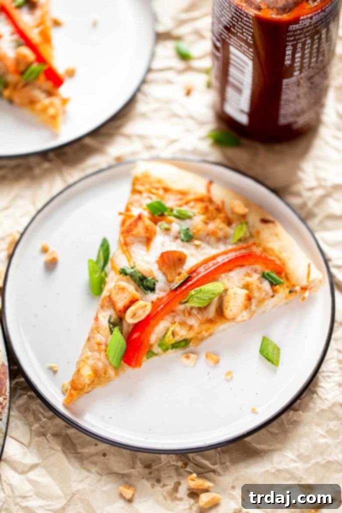 Close-up of a single slice of Thai Chicken Pizza, perfectly baked with golden crust and colorful toppings.
