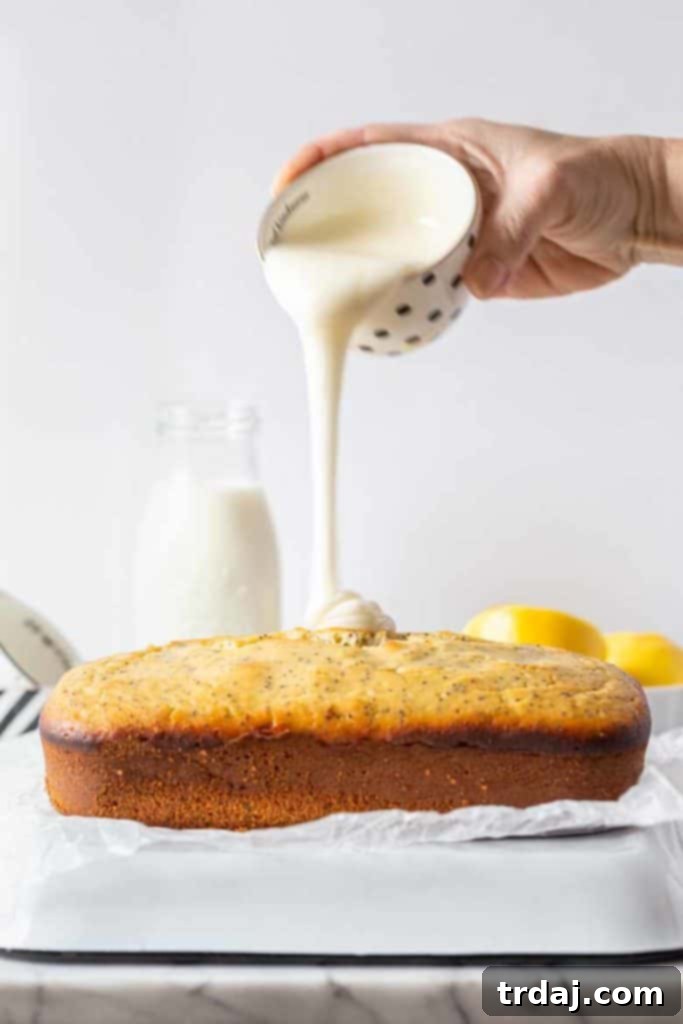 Lemon Poppy Seed Loaf being drizzled generously with a bright, homemade lemon glaze, creating an inviting, glossy finish.