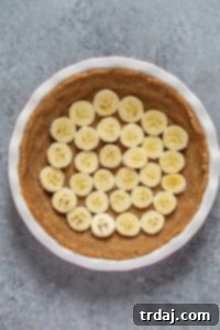 Banana slices placed on top of the no-bake pecan pie crust in a pie pan