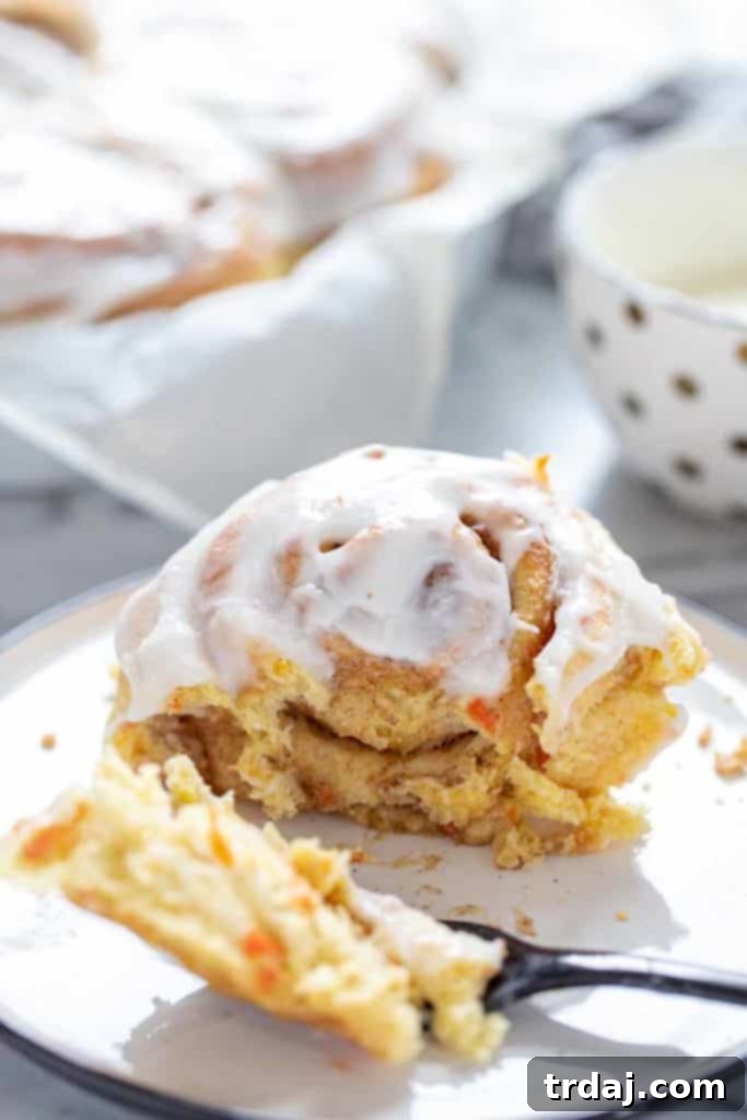 Close-up shot of a single Carrot Cake Cinnamon Roll with Cream Cheese Icing on a plate with a fork