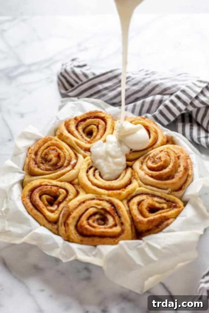 Close-up of a drizzle of thick cream cheese icing on top of warm carrot cake cinnamon rolls