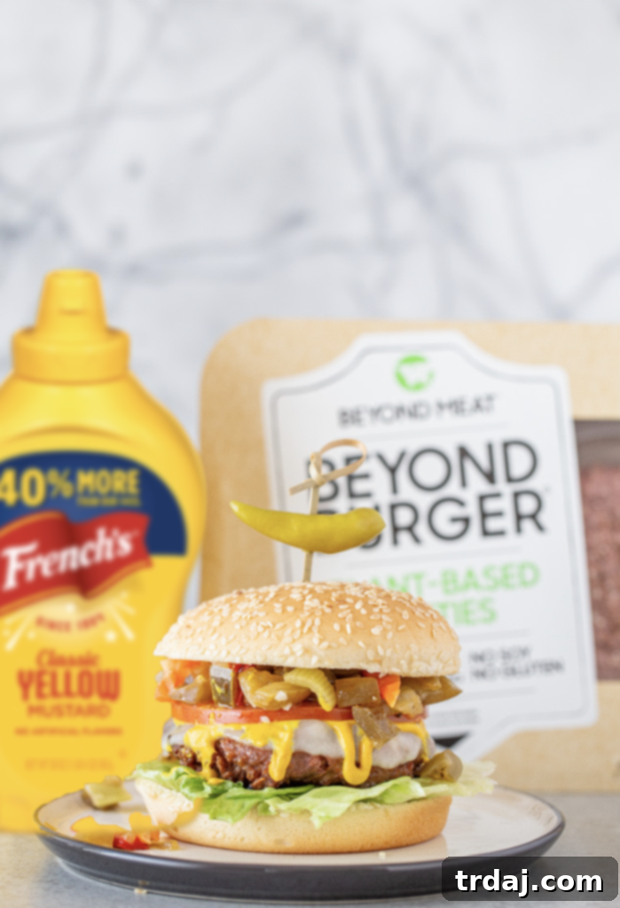 Signature Chicago Beyond Burger 2 A Chicago Style Beyond Burger showcasing a plant-based patty, provolone cheese, mustard, lettuce, tomato, and giardiniera on a seeded bun, accompanied by a package of Beyond Meat Patties and a bottle of French's Yellow Mustard.