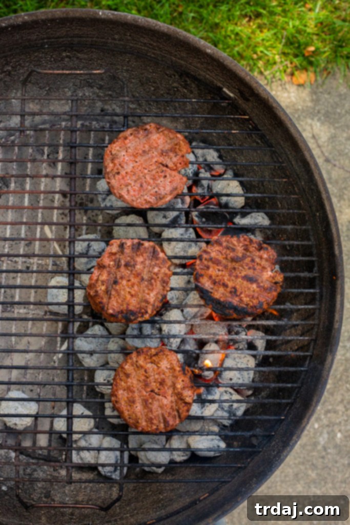 Signature Chicago Beyond Burger 6 Beyond Meat plant-based burger patties sizzling on an outdoor charcoal grill, with a delicious char developing on their surface, ready for toppings.