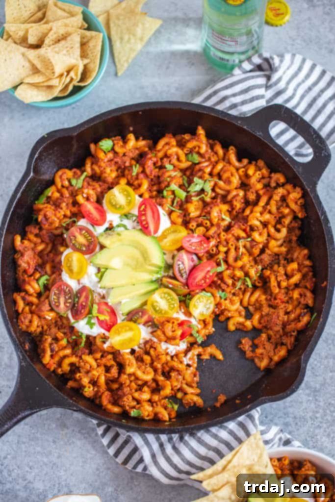 Healthier One Pan Taco Pasta in cast iron pan topped with a generous dollop of sour cream, fresh diced tomatoes, and creamy avocado slices, ready to be served