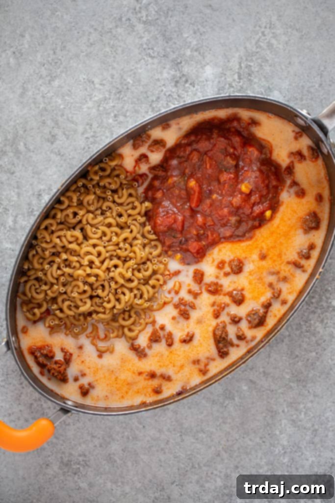 Macaroni pasta, salsa, almond milk, and taco seasoning being added to browned O Organics plant-based crumbles in a large pan for one-pan taco pasta