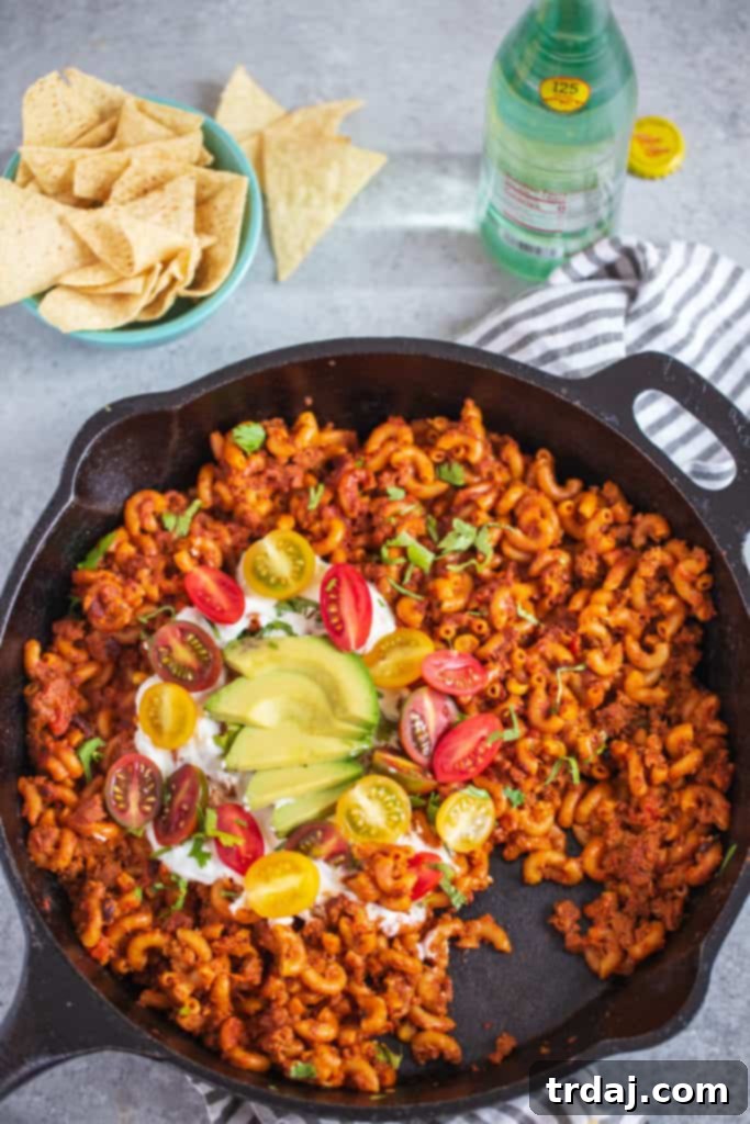 Close-up photography shot of Healthier One Pan Taco Pasta, showcasing the rich, creamy texture of the pasta mixed with plant-based crumbles, black beans, and corn, with melted cheese and fresh herbs visible