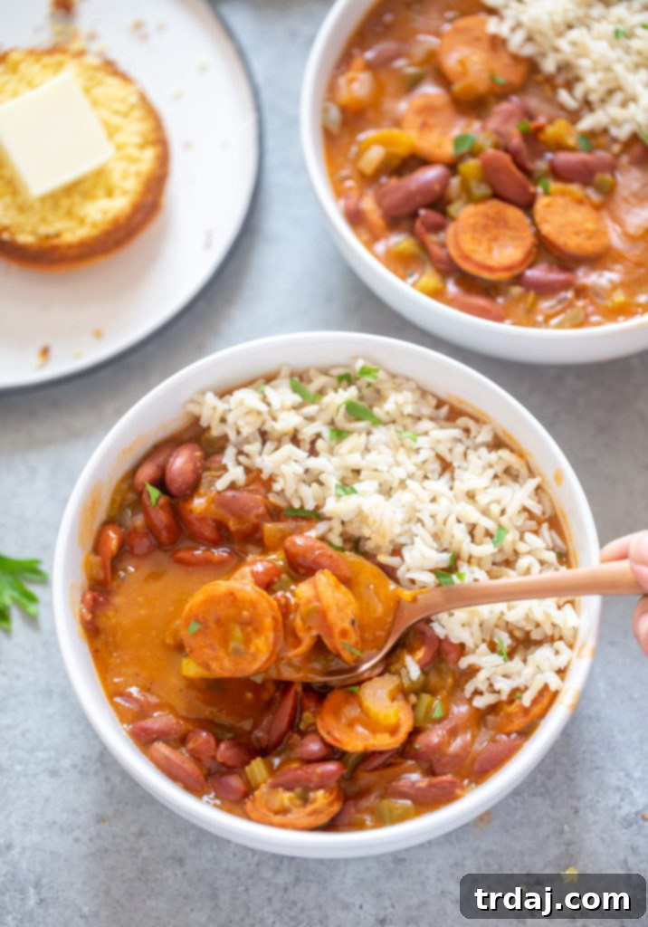 Flavorful and rich, with andouille sausage and hearty vegetables, this One Pan Easy Red Beans and Rice is pure comfort food and on the table in less than 30 minutes! A close-up shot of a spoon lifting a piece of tender andouille sausage from a bowl of succulent red beans and rice, showcasing the delicious texture and rich sauce.