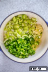 Effortless Red Beans and Rice 2 Freshly diced green bell pepper, yellow onion, celery, and garlic are gently sautéing in olive oil within a sauce pot, releasing their fragrant aromas and softening to form the flavorful base of the dish.