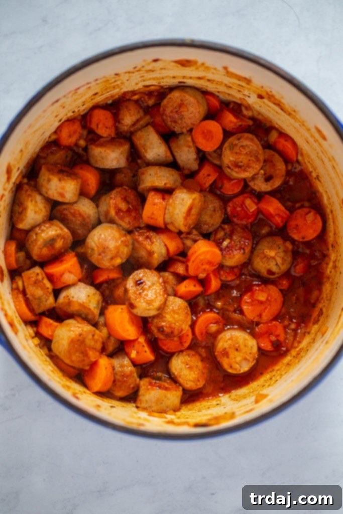 Chicken stock and diced tomatoes added to the pot with sausage, vegetables, and seasonings, coming to a boil