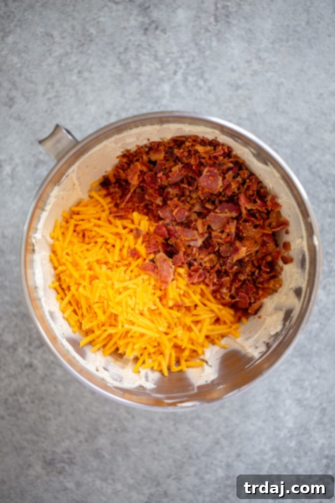 The mixing bowl now contains cream cheese, Worcestershire sauce, seasonings, crispy bacon pieces, and shredded cheddar cheese, all ready to be combined.