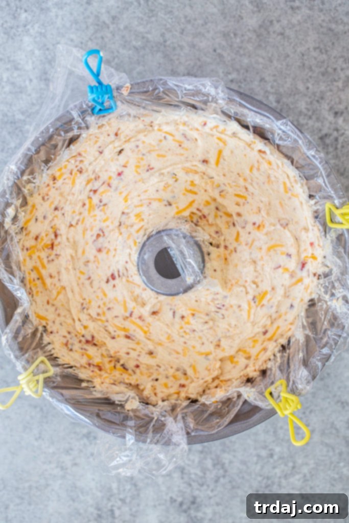 Plastic wrap is placed in a Bundt pan, and the cheese mixture is spooned inside, smoothed, and prepared for refrigeration.