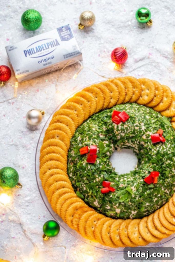 A beautiful side shot of the Bacon Cheddar Cheese Ball Wreath, garnished with parsley and red bell pepper, set on a platter with small festive ornaments and string lights.