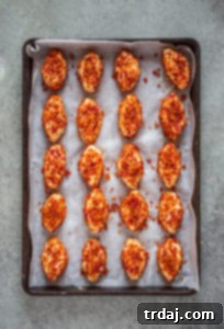 Placing bacon-coated cheese footballs back onto the parchment-lined sheet, ready for final decoration and chilling.