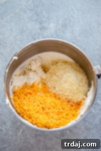 Folding in shredded sharp cheddar and grated Parmesan cheeses into the cream cheese mixture until just combined.