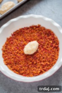 Carefully rolling the shaped cream cheese footballs in crumbled cooked bacon for a savory, crispy coating.