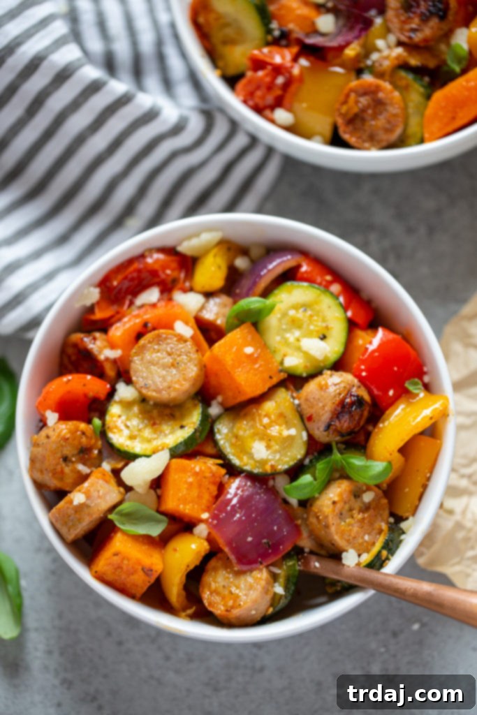 A closer look at a beautifully arranged bowl featuring golden-brown chicken sausages and an array of roasted vegetables, artfully topped with fragrant fresh basil and a generous sprinkle of Parmesan cheese, highlighting the dish's freshness.