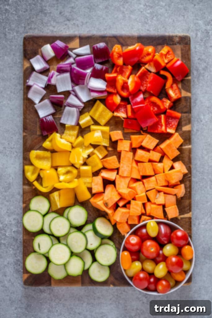 A cutting board laden with freshly chopped red bell peppers, yellow bell peppers, red onions, zucchini slices, and vibrant cherry tomatoes, all prepped and ready for roasting.