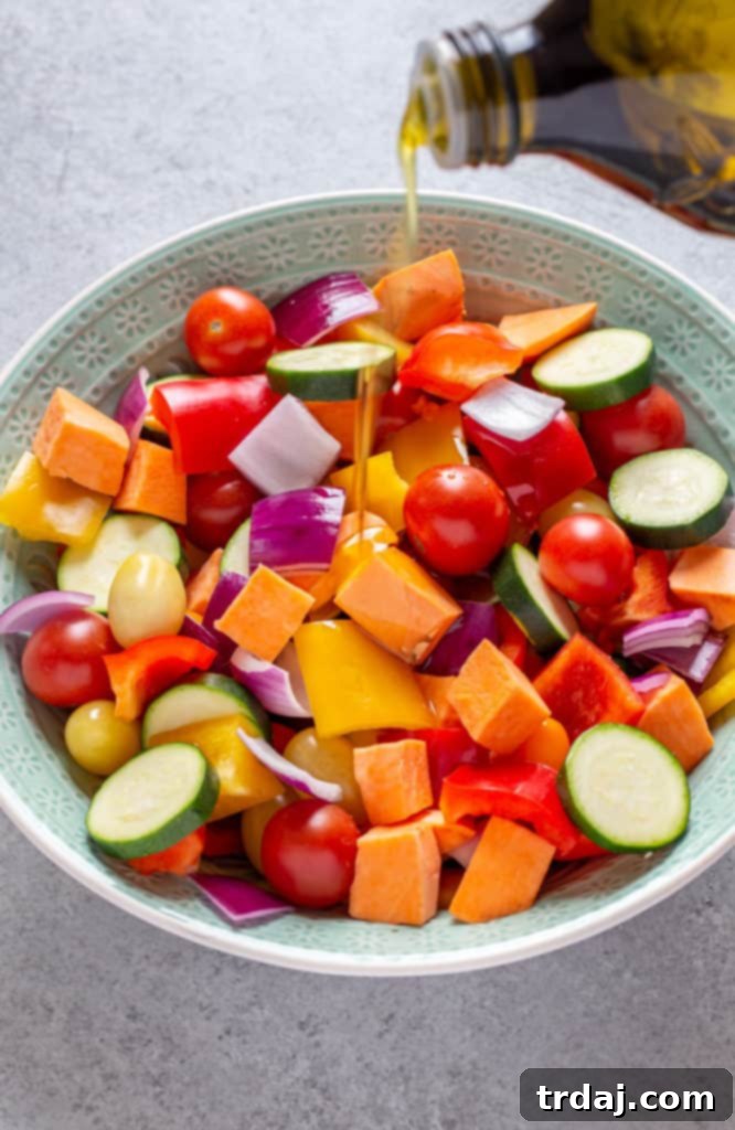 A vibrant collection of chopped vegetables, including bell peppers, onions, zucchini, and cherry tomatoes, perfectly seasoned and glistening with a drizzle of extra virgin olilve oil in a large mixing bowl, ready for the sheet pan.